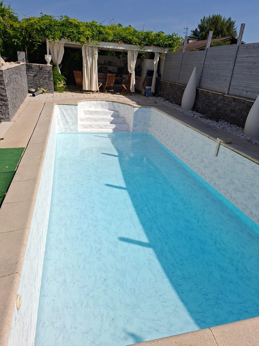 Piscine rénovée en liner marbré blanc avec pergola et pool house